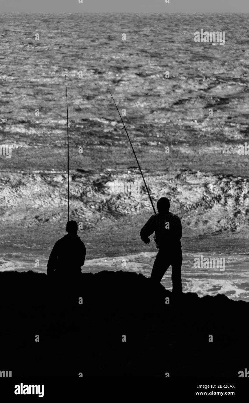 Silhouette of two fishermen is fishing with long rods Stock Photo