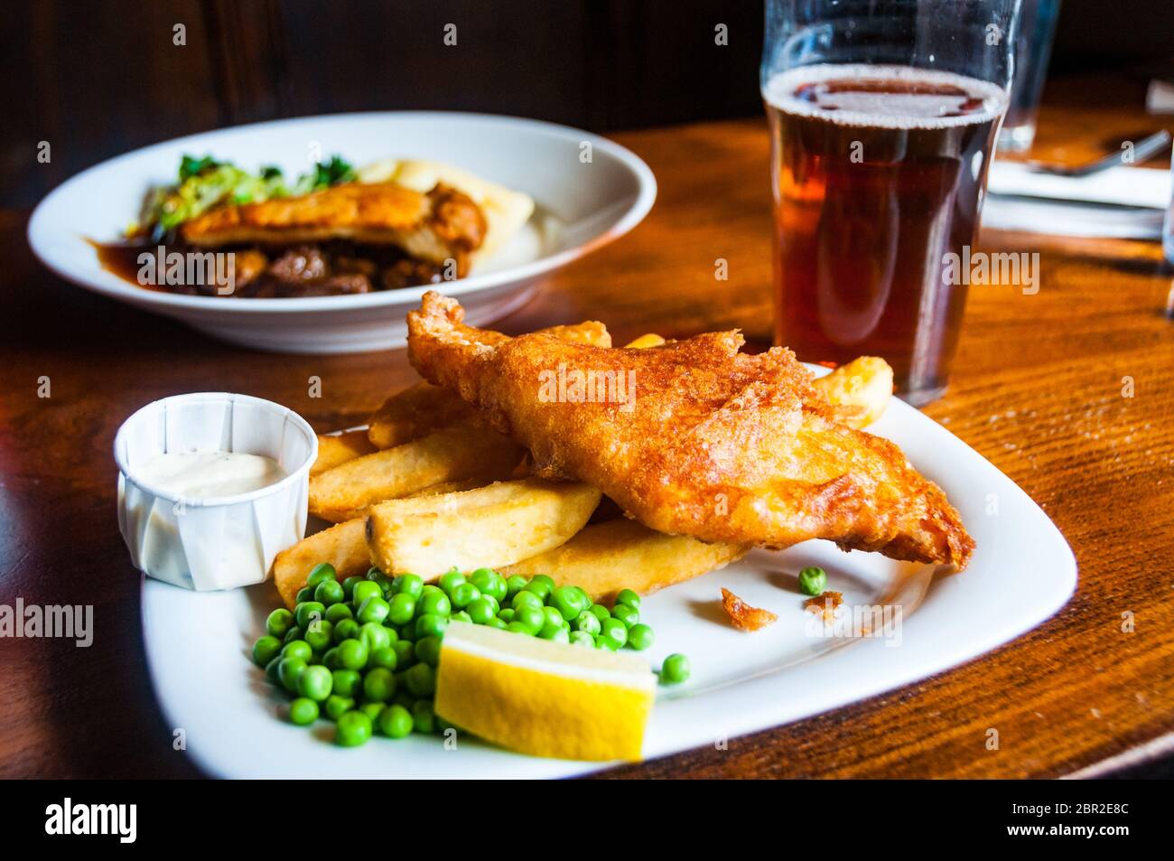 A traditional British pub meal with fish and chips and a steak and mushroom pie along with a pint of bitter. Stock Photo