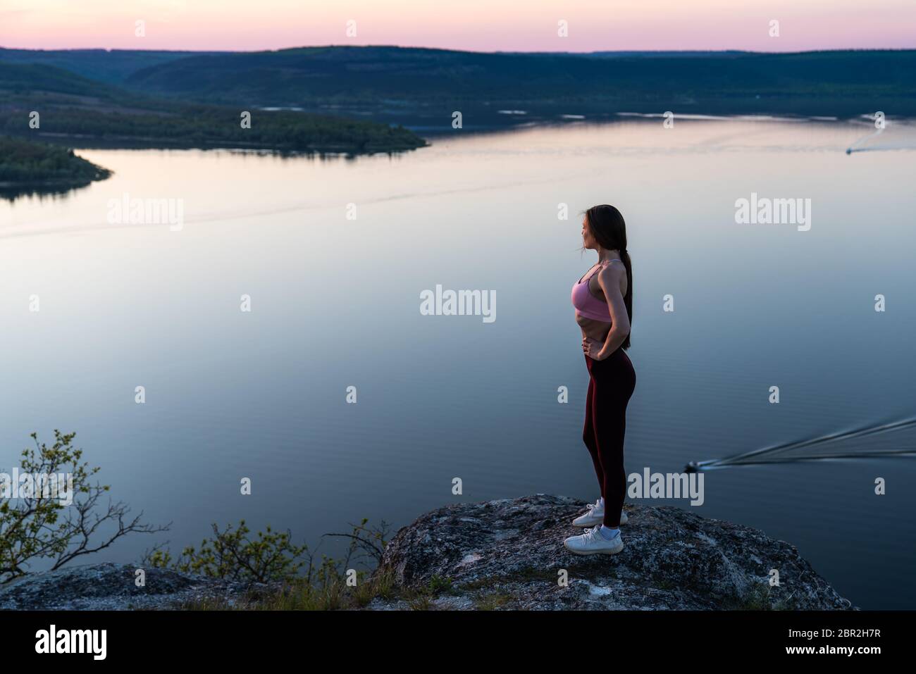 Pretty sporty girl stay on the top of the mountain and looking to the horizon with beautiful river background Stock Photo