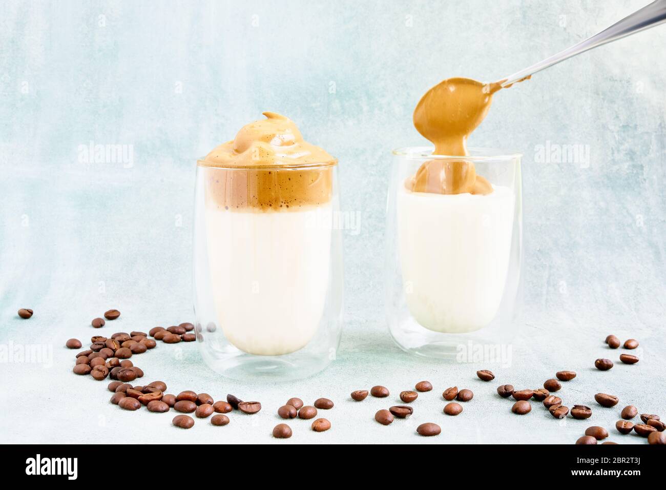 Trendy homemade Dalgona coffee in glass on blue background. Recipe of popular Korean drink latte with foam of instant coffee. DIY, instruction. Stock Photo