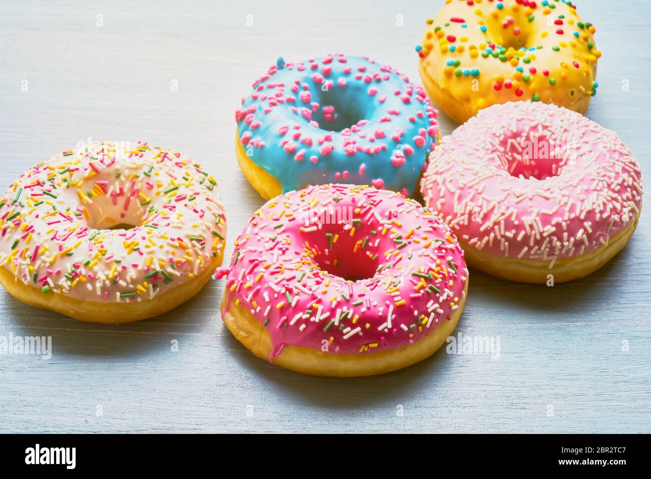 Assorted donuts with colorful frosted, pink glaze and sprinkles on blue ...