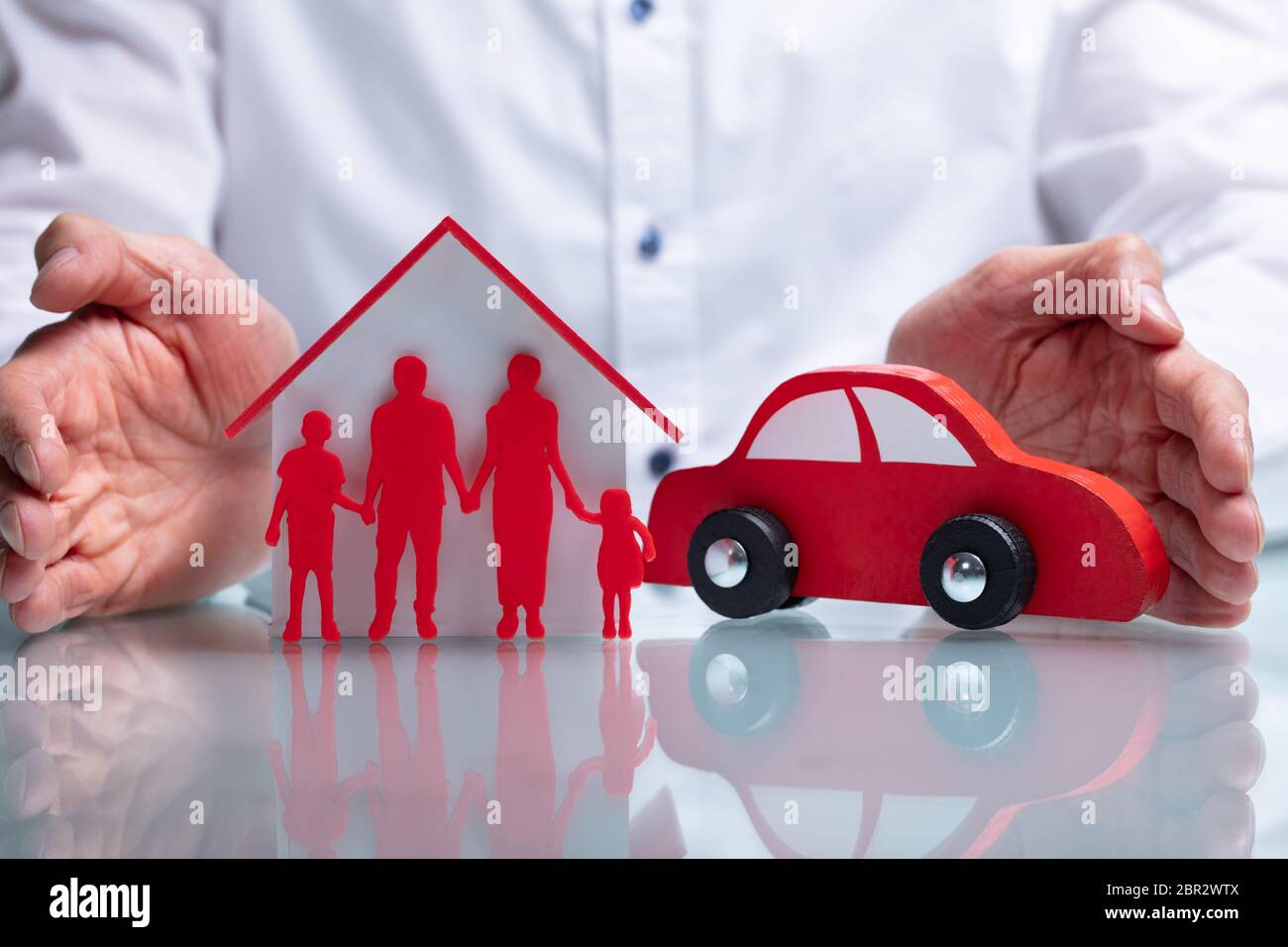 Photo Of Businessman Protecting Family Figure, House Model And Car Stock Photo