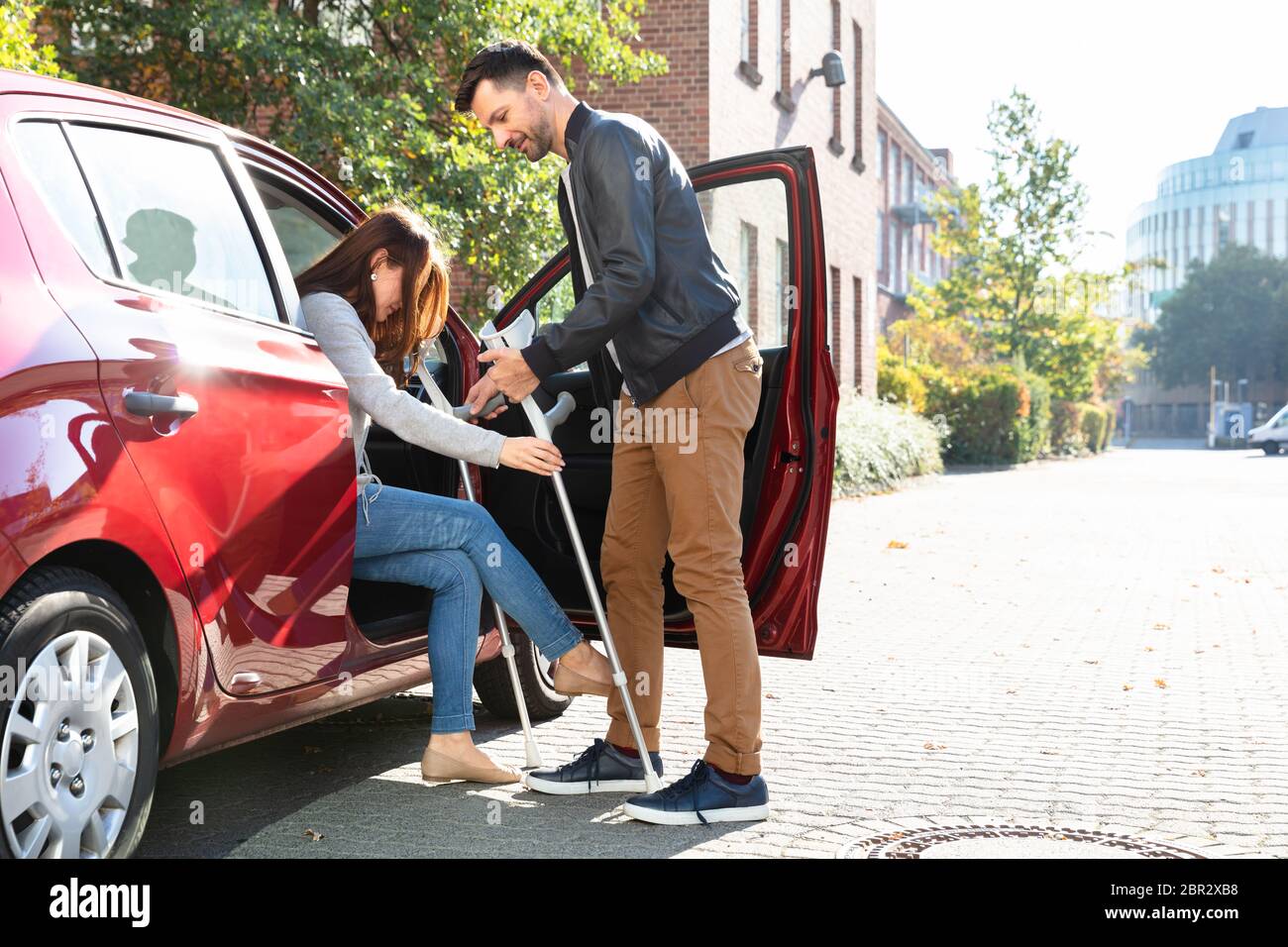 Smiling Young Husband Helping Her Disabled Wife With Crutches To Get