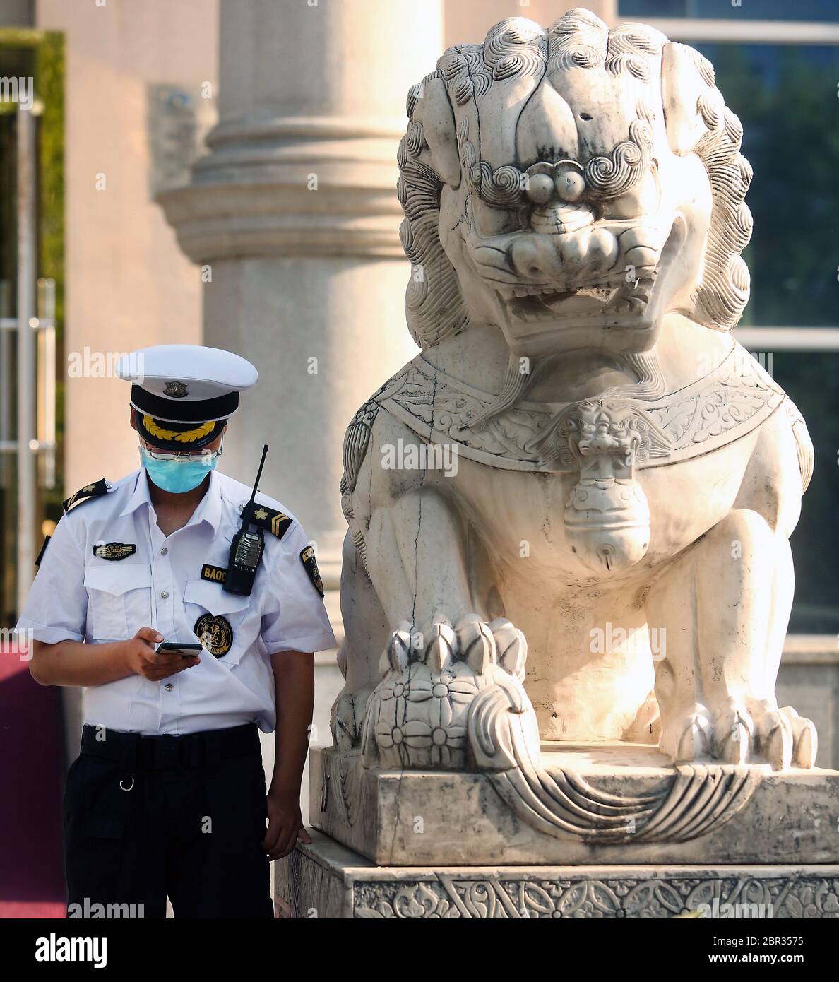 Beijing, China. 20th May, 2020. A Chinese government security guard uses his phone next to a traditional 'Guardian Lion' placed outside a bank in Beijing on Wednesday, May 20, 2020. Wuhan, a city of 11 million, where the Covid-19 pandemic originated, reported new cases over the weekend, its first new infections in over a month. China is aggressively investigating the new cluster, announcing a plan to test the entire city in 10 days. Photo by Stephen Shaver/UPI Credit: UPI/Alamy Live News Stock Photo