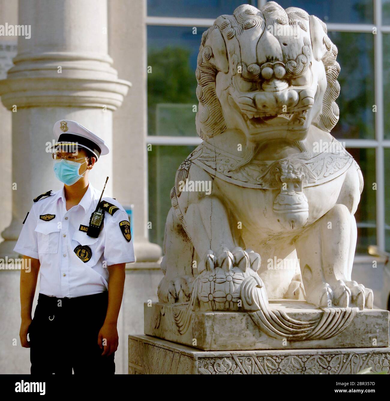 Beijing, China. 20th May, 2020. A Chinese government security guard stands next to a traditional 'Guardian Lion' placed outside a bank in Beijing on Wednesday, May 20, 2020. Wuhan, a city of 11 million, where the Covid-19 pandemic originated, reported new cases over the weekend, its first new infections in over a month. China is aggressively investigating the new cluster, announcing a plan to test the entire city in 10 days. Photo by Stephen Shaver/UPI Credit: UPI/Alamy Live News Stock Photo