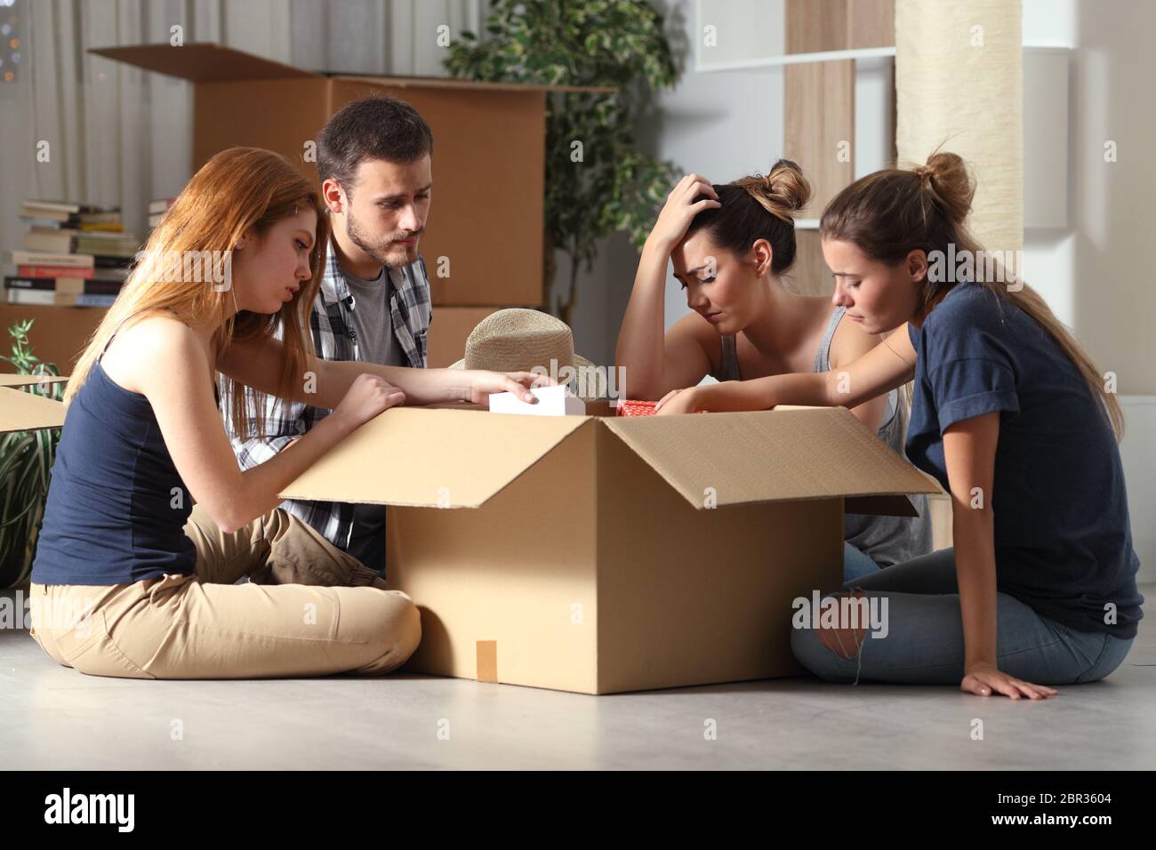 Sad evicted roommates moving home boxing belongings sitting on the floor in the night Stock Photo