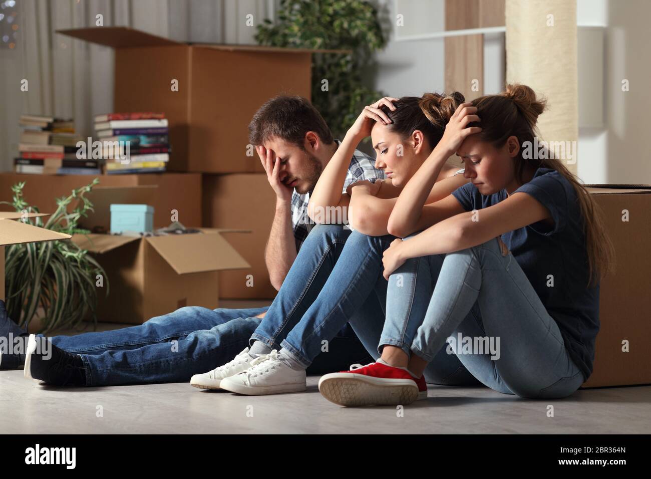 Three sad evicted roommates moving home complaining sitting on the floor Stock Photo