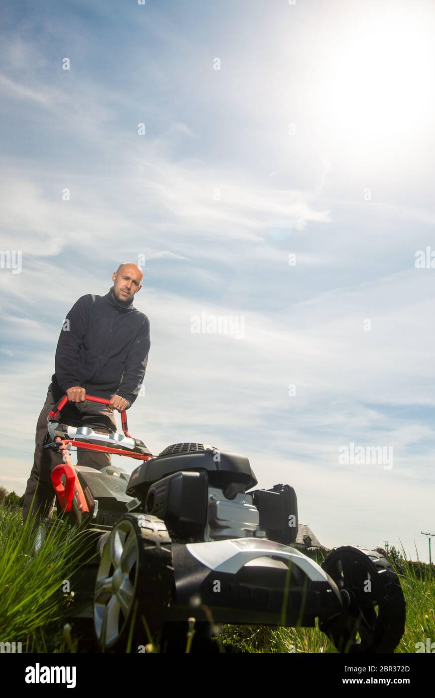 Man mowing, cutting grass on his huge garden yard, green field by the motor garden mower, gardening concept Stock Photo