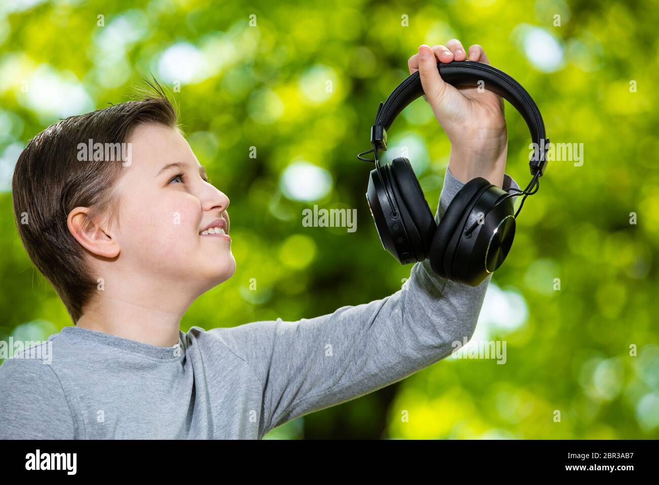 Boy listening a music by huge headphones in outside forest, bokeh background Stock Photo