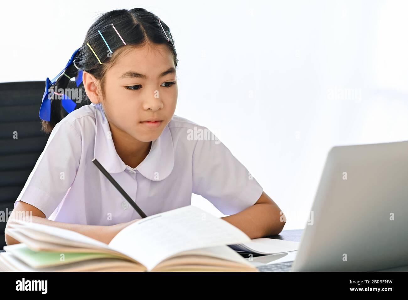 School girl in a uniform sitting near a laptop and looking at the screen leaning or exam with online e-learning teacher Stock Photo