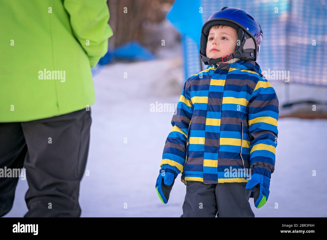 Cute little Caucasian ski adept looking at and listening to his ski instructor on a slope in winter Stock Photo