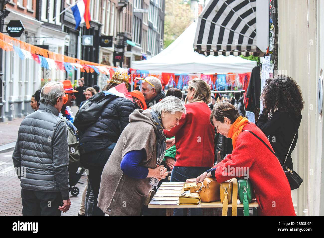 Amsterdam, Netherlands - April 27, 2019: People buying and selling on the traditional flea market during the Kings day, Koningsdag. Streets decorated with Dutch flags and national colors. Stock Photo