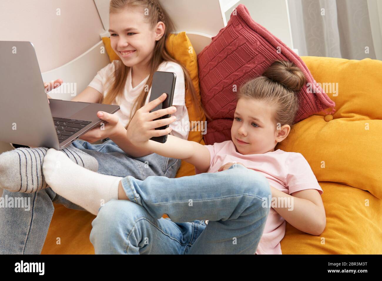 Two little sisters using laptop lying on bed at home Stock Photo - Alamy