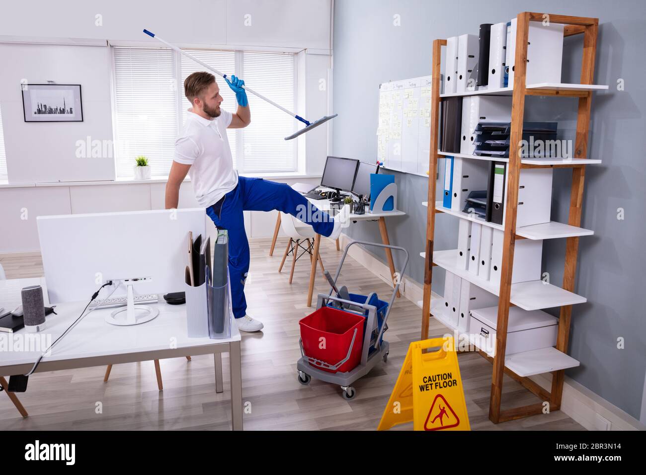 Man Janitor Slipping While Mopping Floor In Modern Office Stock Photo