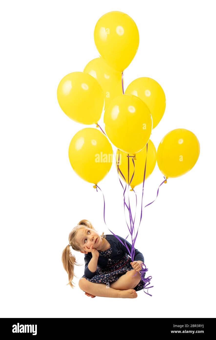 sitting little girl holding yellow balloons in her hand. isolated on white. hair with pigtails, bored expression. Stock Photo