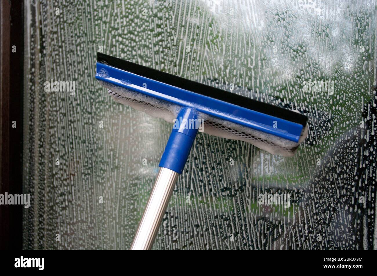 Cleaning window using a squilgee to wash glass. Stock Photo