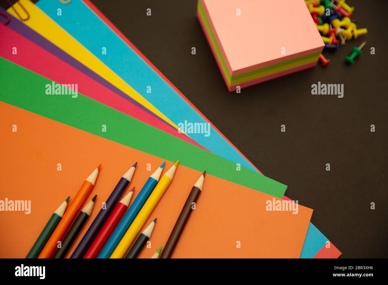 Pencils, multi-colored paper and paper clips on a black background Stock Photo