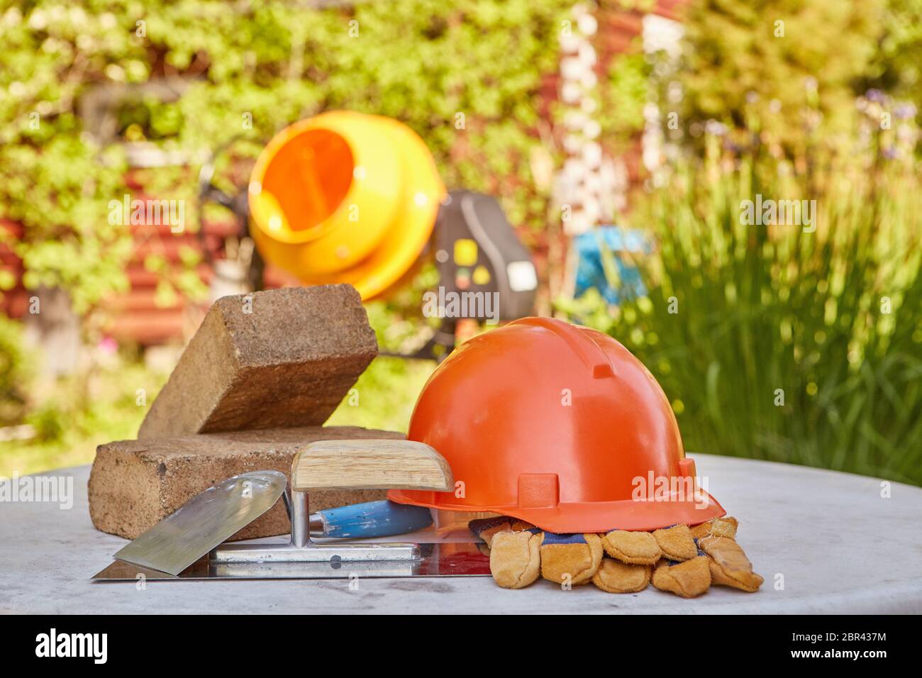 Construction concept. Bricks, tools, hard hat, gloves and concrete mixer. Outdoors Stock Photo