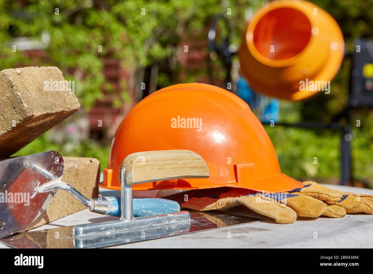 Construction concept. Bricks, tools, hard hat, gloves and concrete mixer. Outdoors Stock Photo