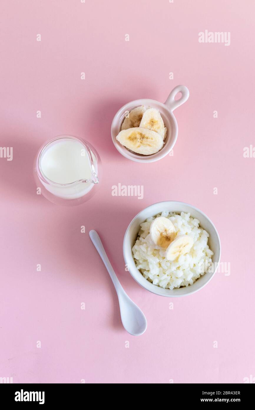 Top view of rice milk porridge with banana slices, daughter and milk on a pink background. Vertical photo Stock Photo