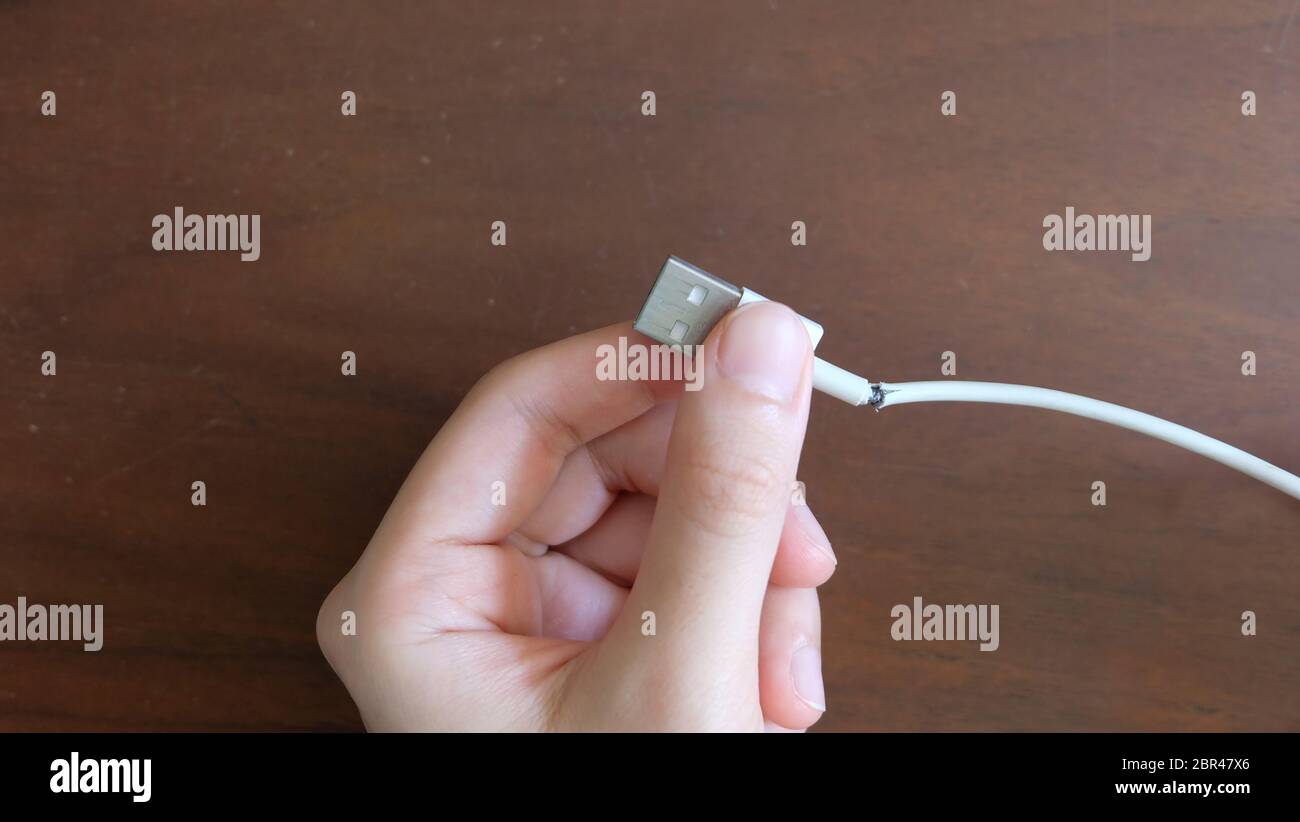 Hand holding a USB cable that is damaged. Stock Photo