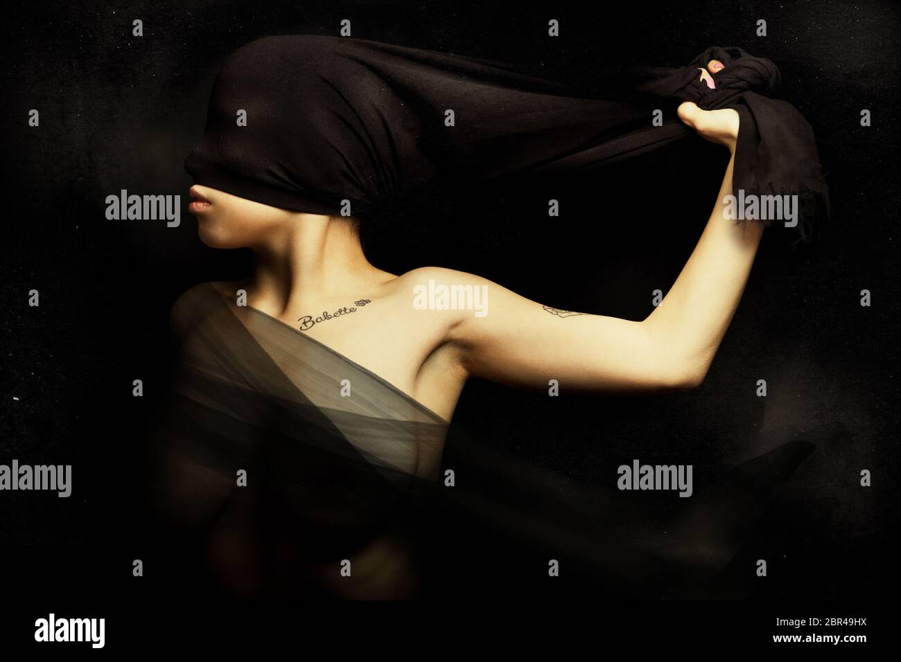 Woman blinded by a cloth hiding face. Rebellion and silence. A young woman is blinded by a cloth pulled from hand. Artistic portrait with black backgr Stock Photo