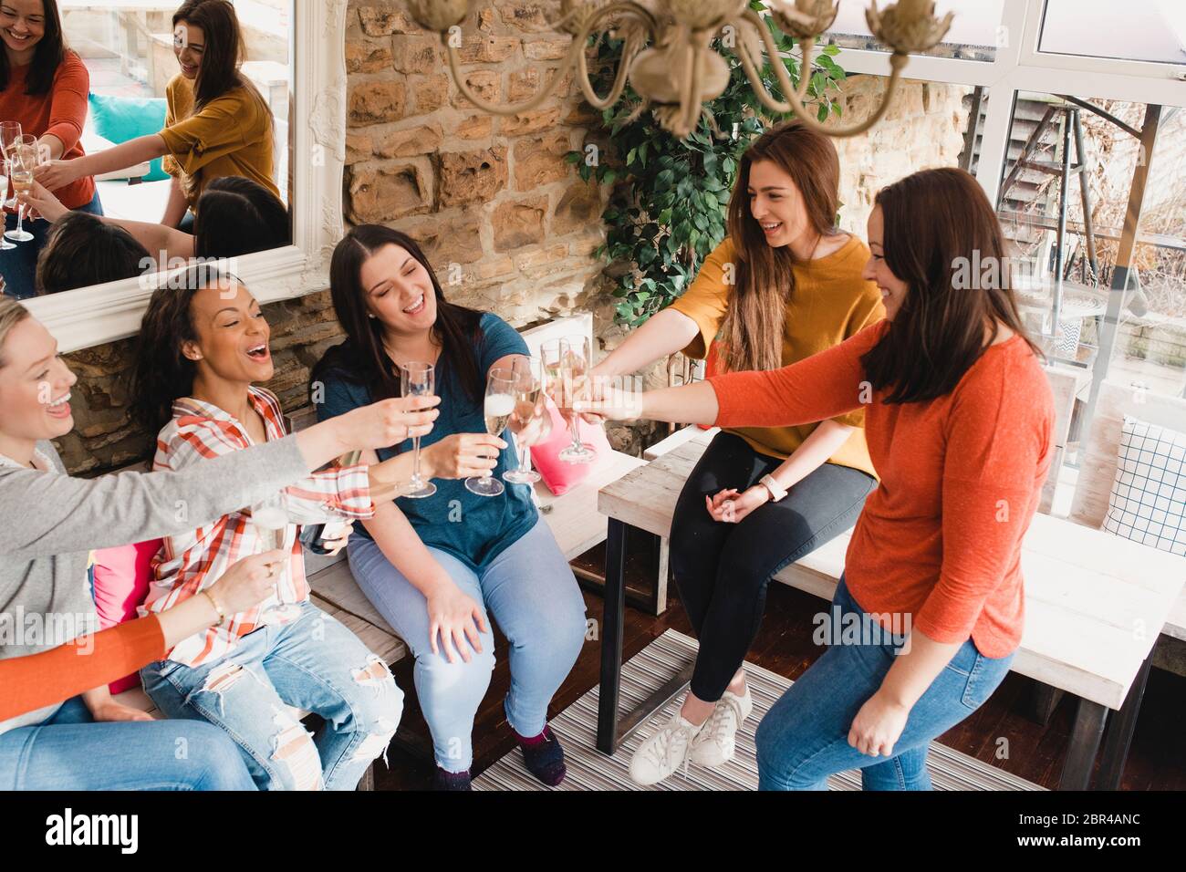 Small group of women with a mixed age range making a celebratory toast with a glass of champage. They are sitting indoors, in a conservatory. Stock Photo
