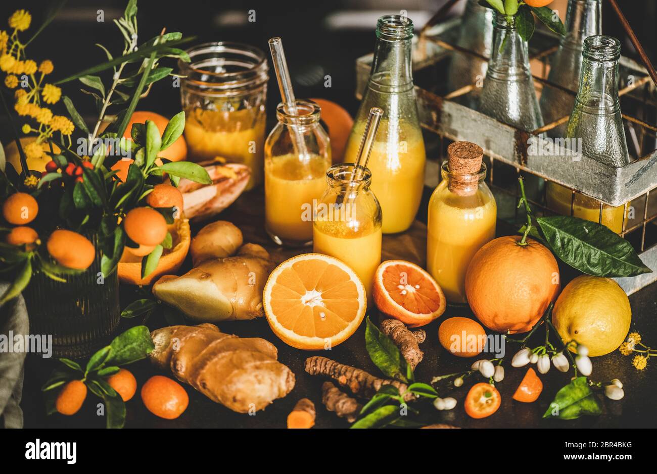 Immune boosting vitamin health defending drink. Turmeric, ginger and citrus juice shots in bottles and fresh ingredients over concrete kitchen counter Stock Photo
