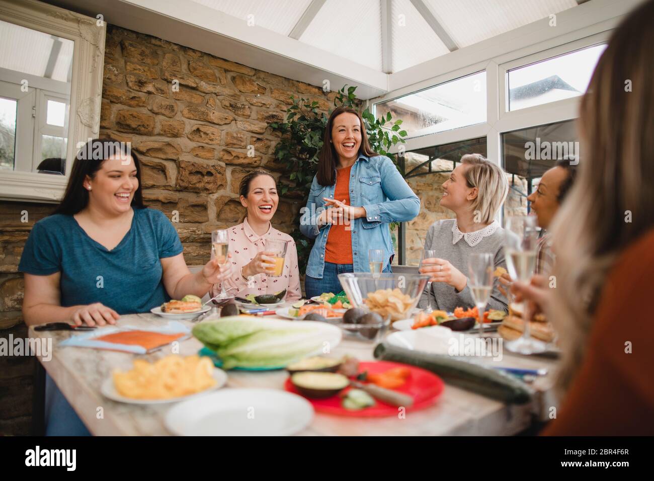 Small group of female friends preparing a healthy lunch inside of a conservatory on a weekend away. Stock Photo