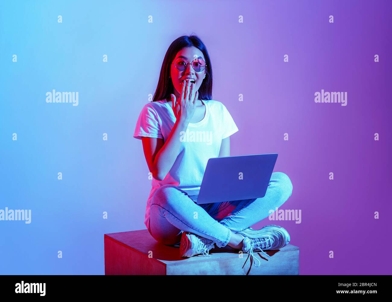 Modern blogger with laptop in workspace. Surprised girl in glasses closes mouth with hand Stock Photo