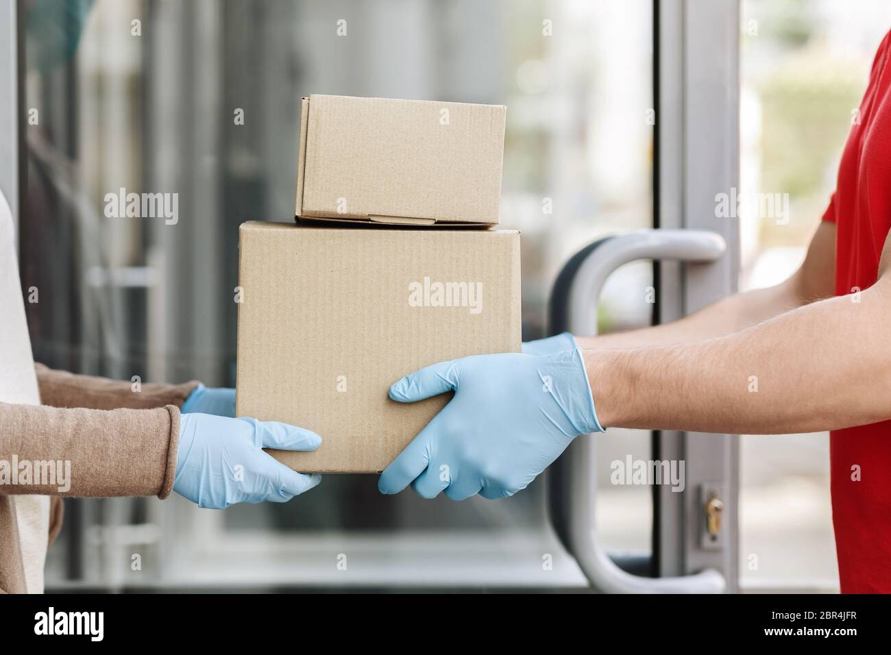 Hands of courier in protective gloves gives boxes to customer at doors Stock Photo