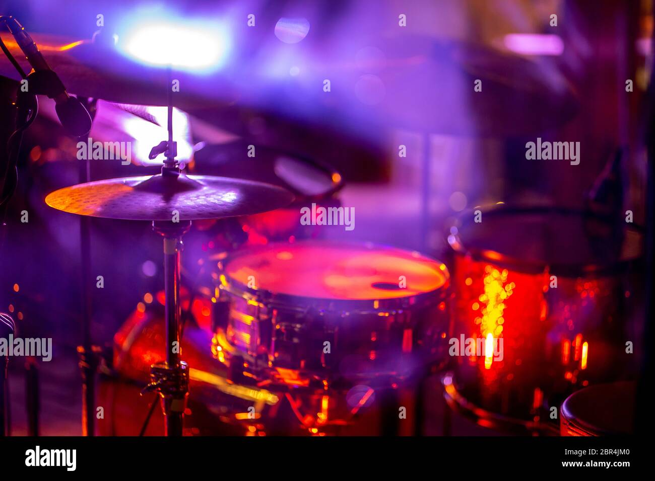 Empty abstract light illuminated stage with drumkit and microphone. Drums in multicolored light during celebrations on stage. Stock Photo