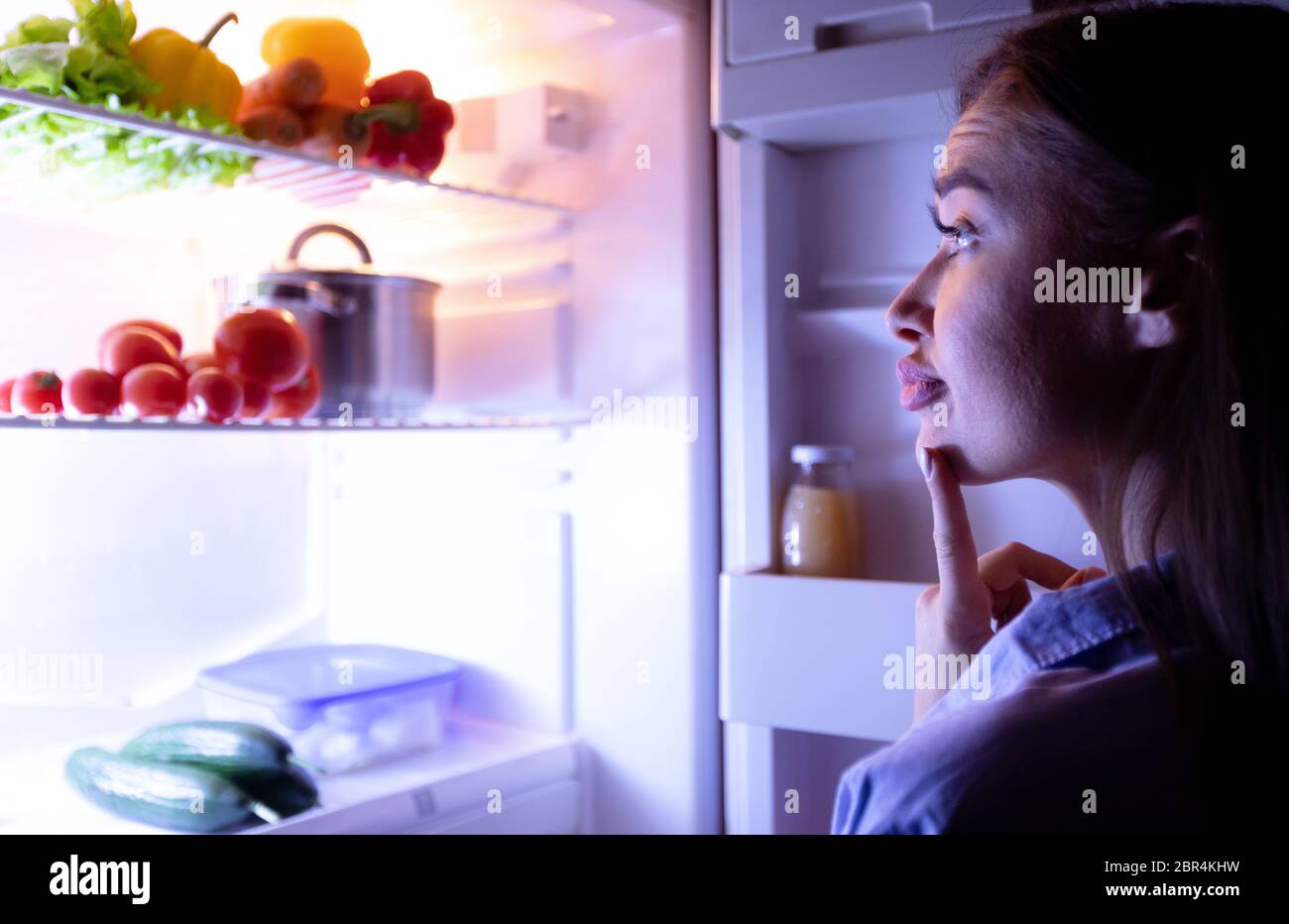 Thoughtful housewife choosing what to eat in fridge in evening Stock Photo