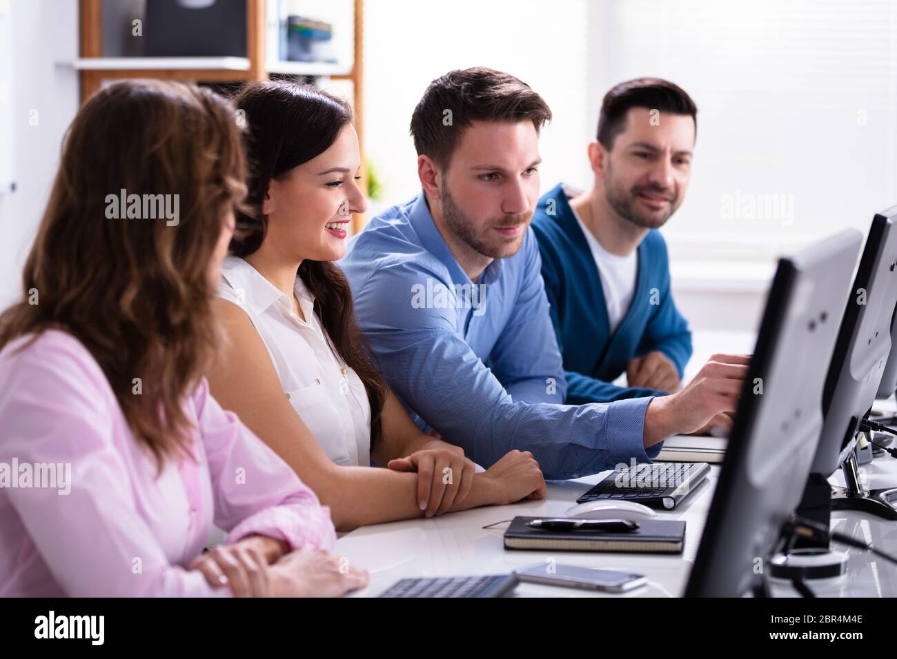Businessman Pointing On Computer Screen While Talking With Her Colleague Stock Photo