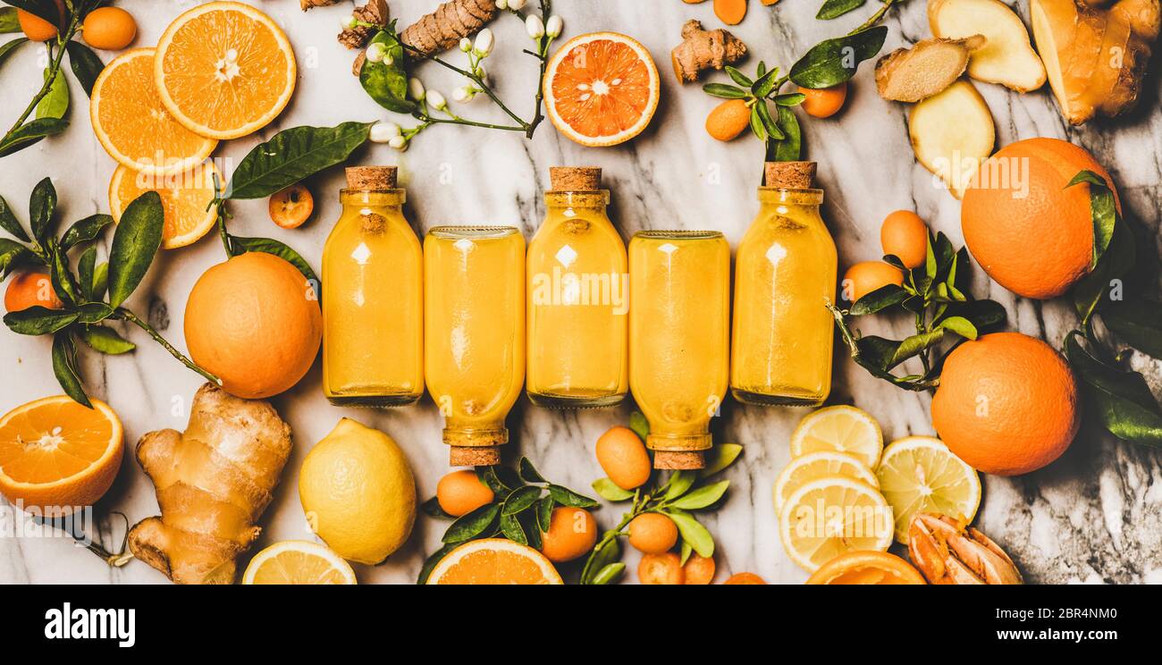 Immune boosting vitamin health defending drink. Flat-lay of fresh turmeric, ginger, citrus juice shot in glass bottles over marble background, top vie Stock Photo