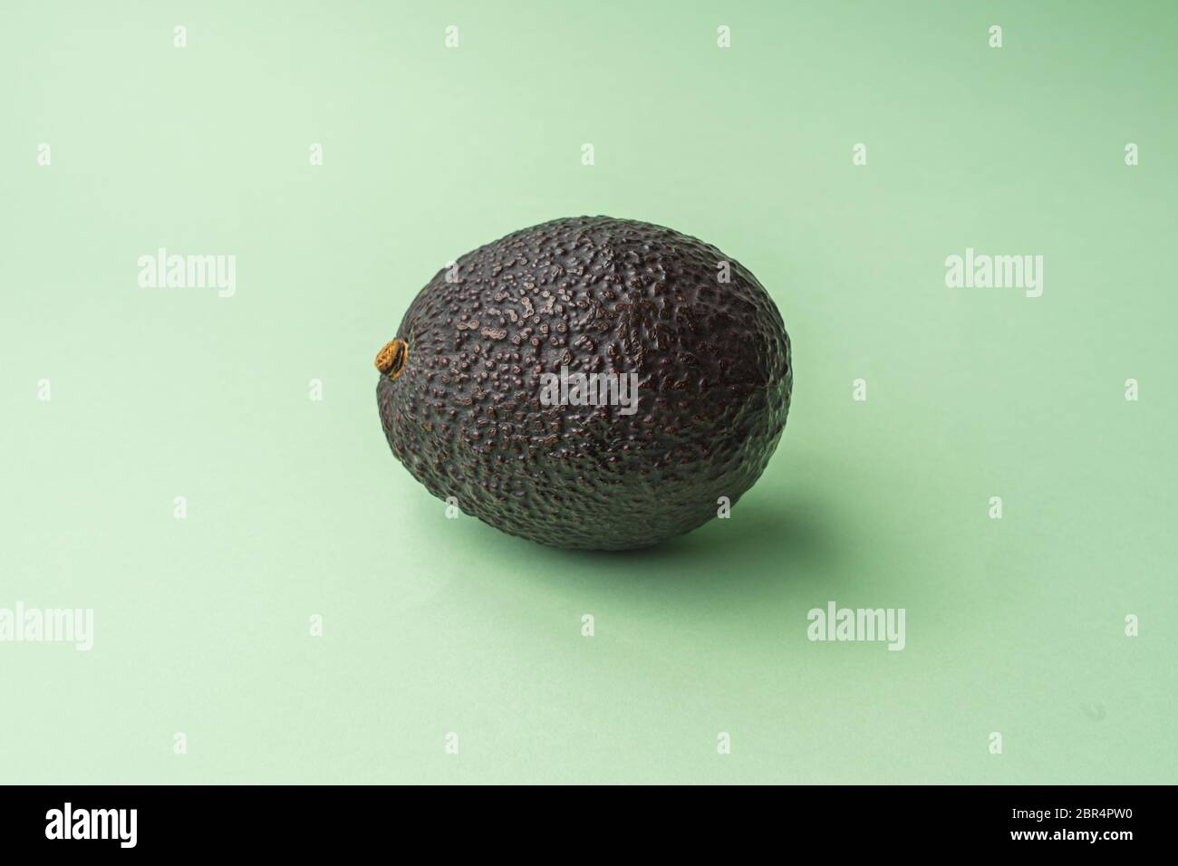 Whole and ripe natural avocado with rough skin located in the center with a green background. Natural fat and raw food Stock Photo