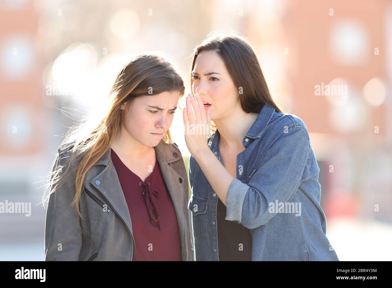 Gossip woman telling secret to her angry friend in the street Stock Photo
