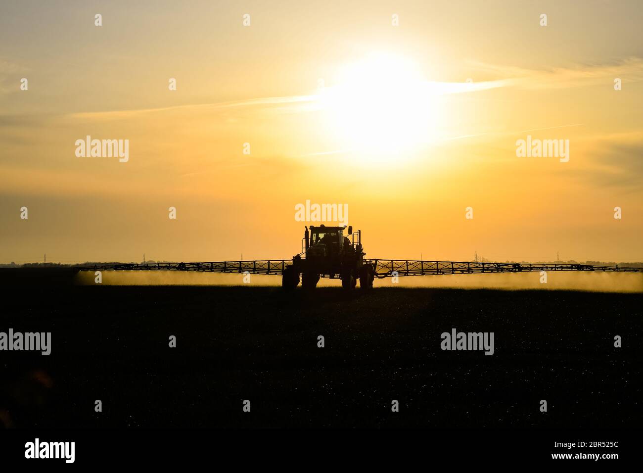 Tractor with the help of a sprayer sprays liquid fertilizers on young wheat in the field. The use of finely dispersed spray chemicals. Tractor on the Stock Photo