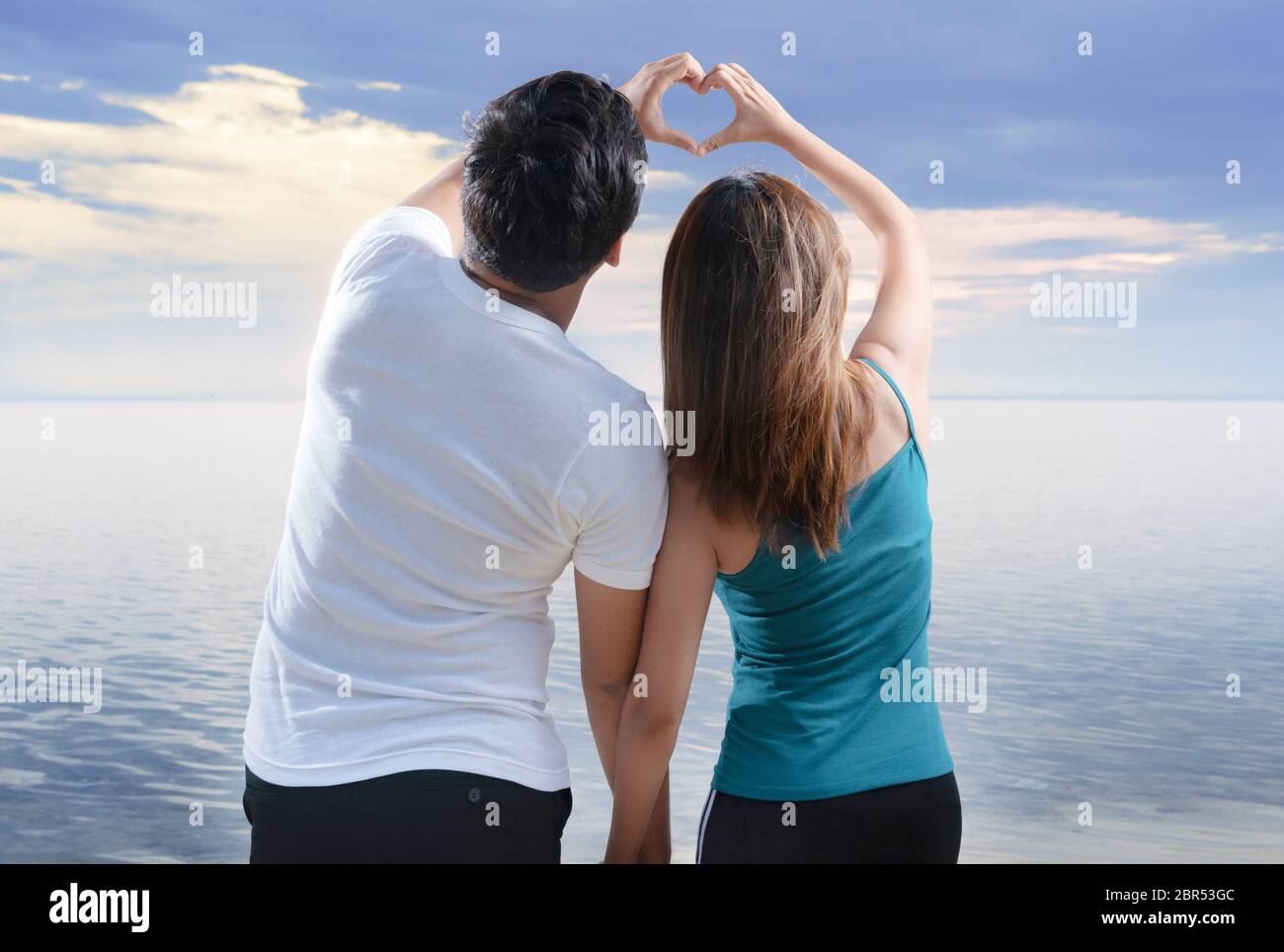 Rear view of asian romantic couple making heart shapes with fingers on ...