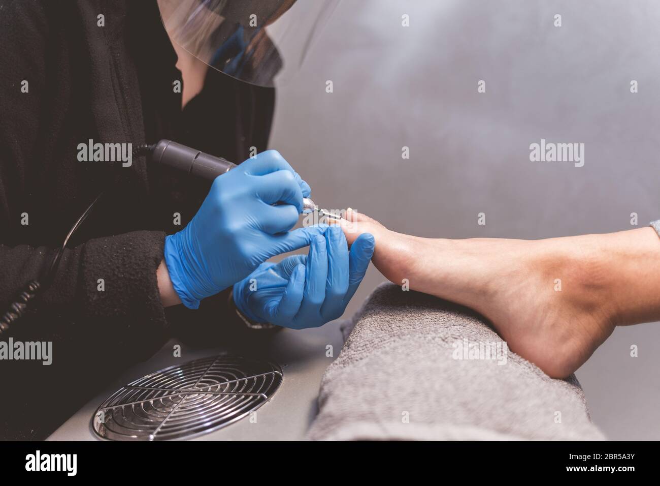 Pedicure master polishes nails with nail file drill before applying