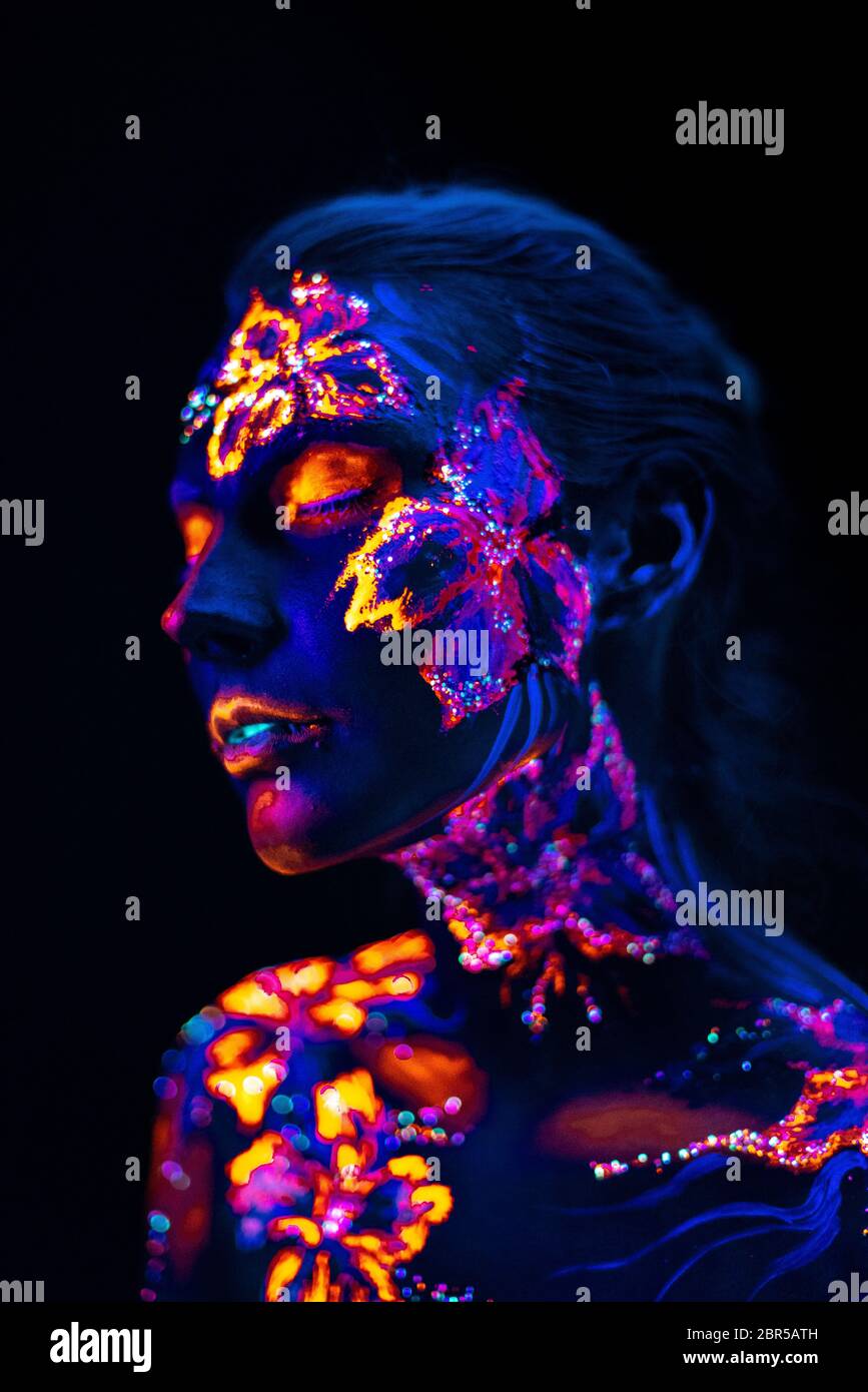 Conceptual face art with shining flowers painted in fluorescent colors isolated on black background Stock Photo