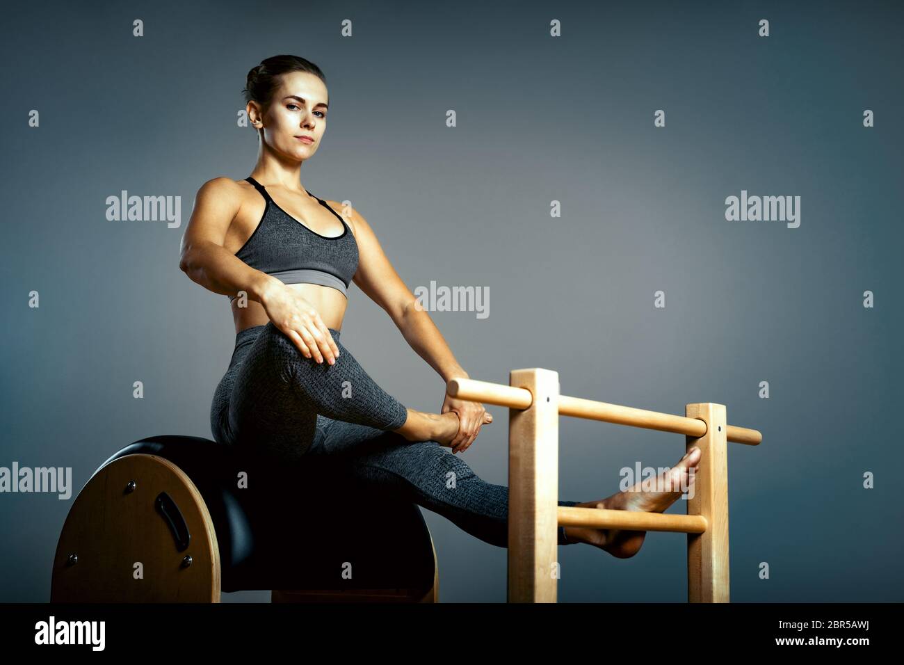 Beautiful woman doing pilates exercise, training on barrels. Barrel