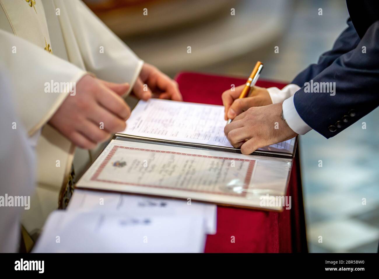 The groom signs documents on registration of marriage in the presence of the pastor. Young couple signs wedding documents in the church during wedding Stock Photo