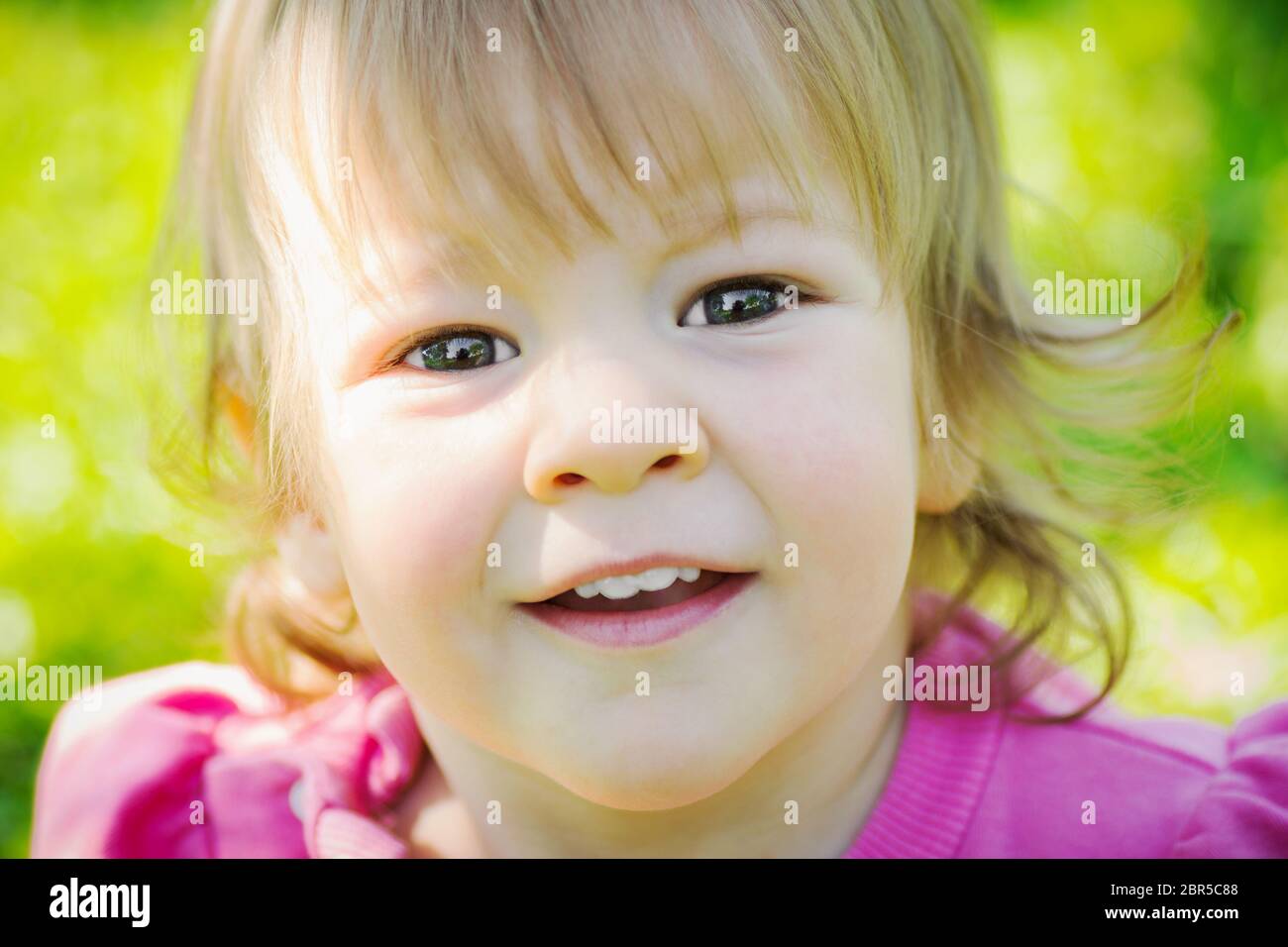 Close-up portrait of happy smiling little girl in pink on green ...