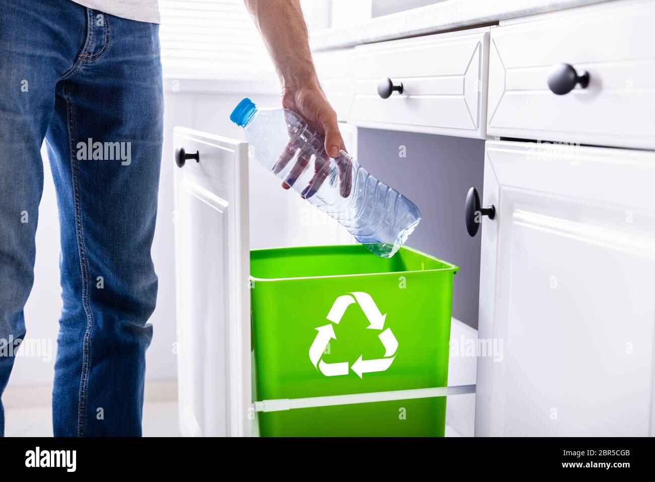 Low Section Of Man Throwing Empty Plastic Bottle In Recycling Bin In