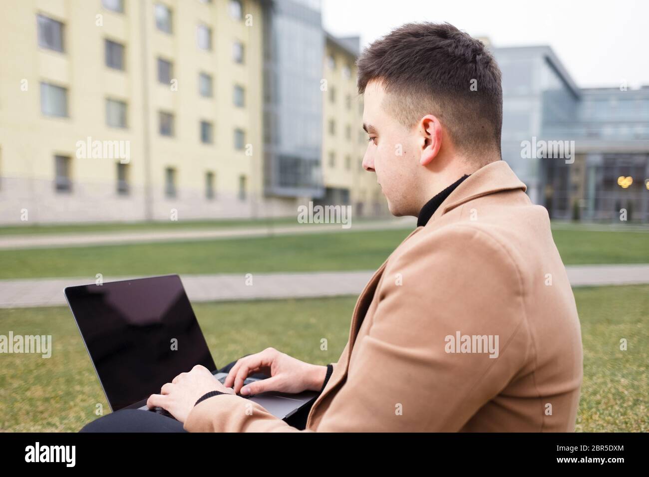 Man works at a laptop while sitting on the grass Stock Photo