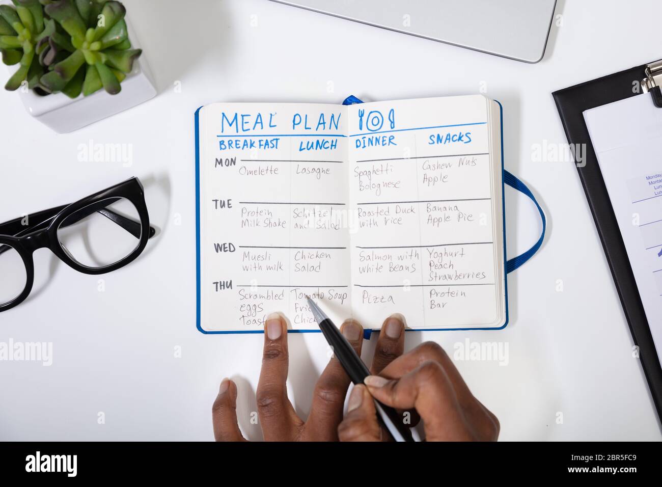 High Angle View Of A Person's Hand Filling Meal Plan On Notebook Stock Photo