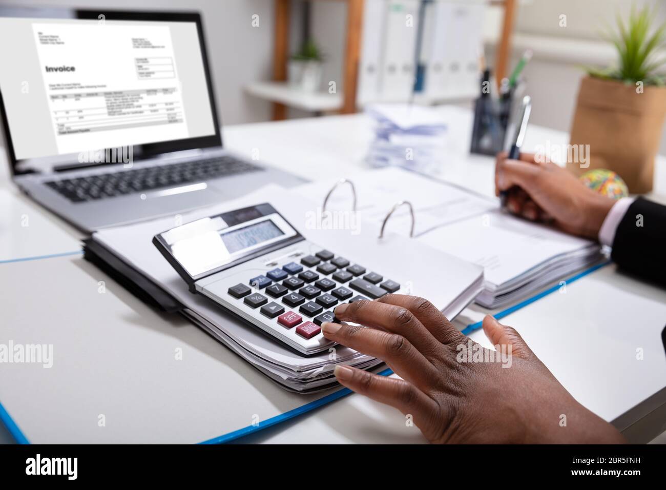 Close-up Of A Businesswoman Calculating Invoice Using Calculator Near Laptop Stock Photo