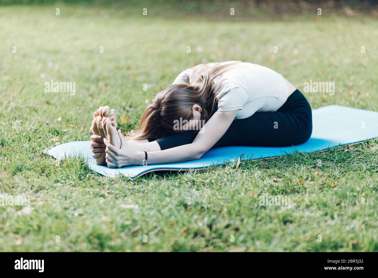 flexible sporty woman doing stretching yoga in park Stock Photo