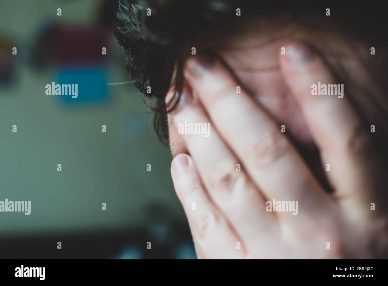 An overwhelmed man covers his face with his hand. Stock Photo